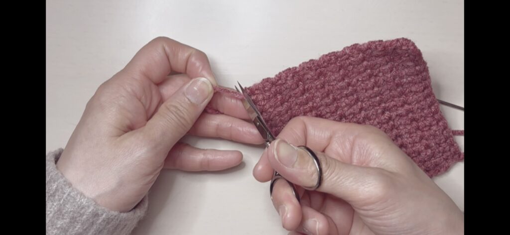 往復編みのコースターの作品が完成し、最後の糸を切る画像